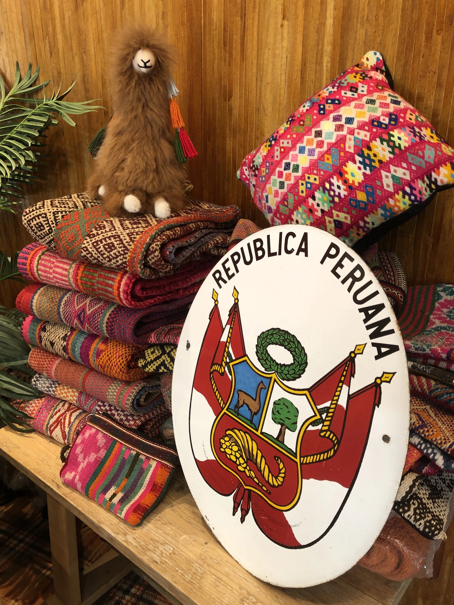 Stack of colorful Peruvian vintage handwoven wool rugs with decorative ethnic pillow, Peru shield and alpaca figure