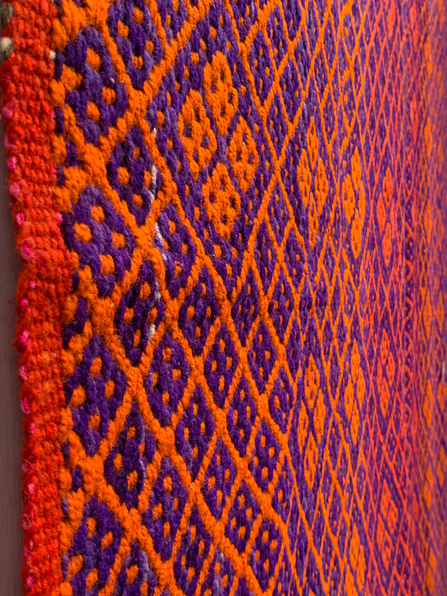 Peruvian vintage handwoven wool rug, detailed close-up  from the side of tightly woven Andean diamond patterns in orange and purple.