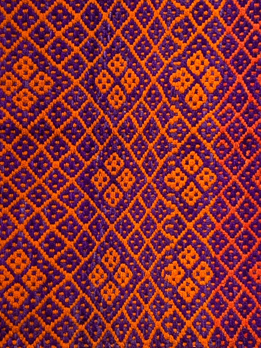 Peruvian handwoven wool rug, medium close-up of orange and purple colours with Andean diamond motifs showing detailed weaving.