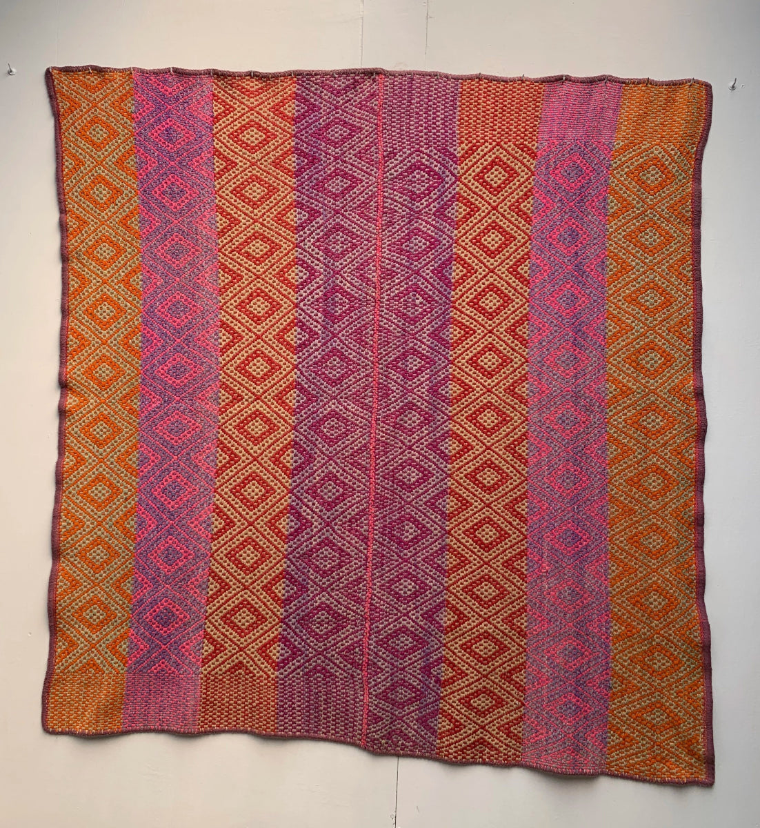 Full view of a Peruvian vintage handwoven wool rug featuring red, orange and purple with Andean diamond patterns made with natural dyes.
