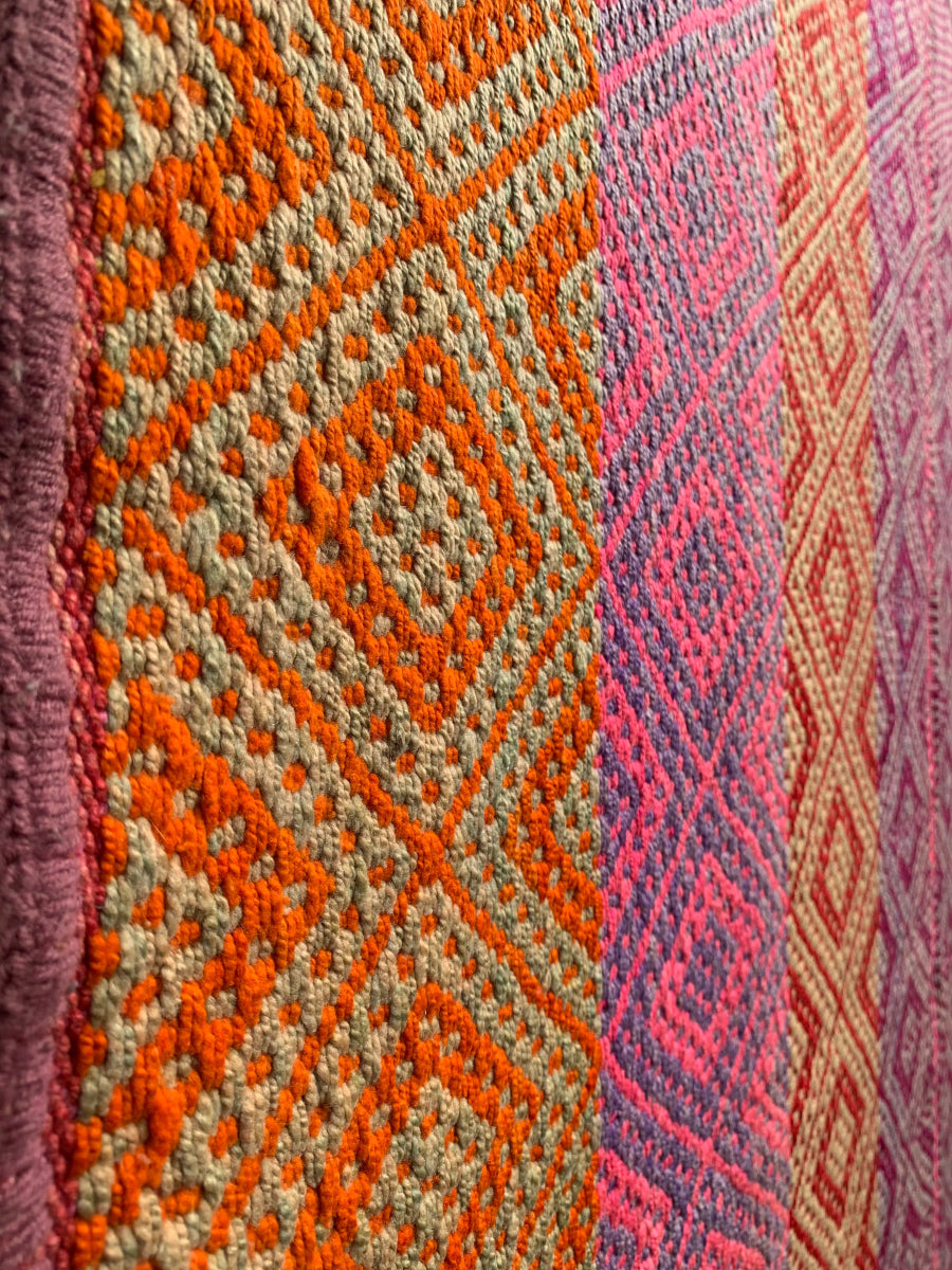 Peruvian vintage handwoven wool rug, detailed close-up  from the side of tightly woven Andean diamond patterns in red, orange and purple.
