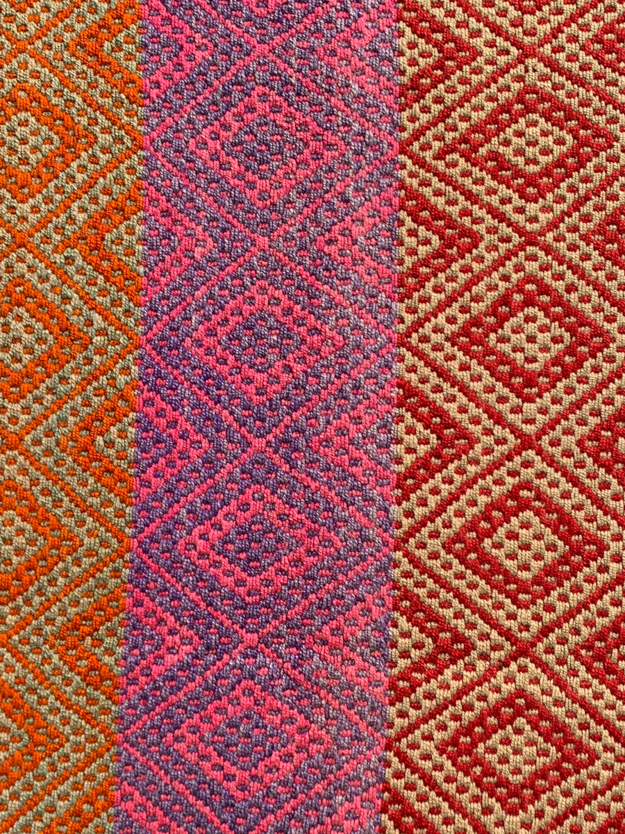 Peruvian handwoven wool rug, medium close-up of red, orange and purple with Andean diamond motifs showing detailed weaving.