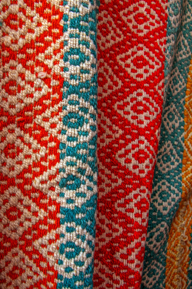 Peruvian vintage handwoven wool rug, detailed close-up of tightly woven Andean diamond patterns in turquoise, red and yellow.