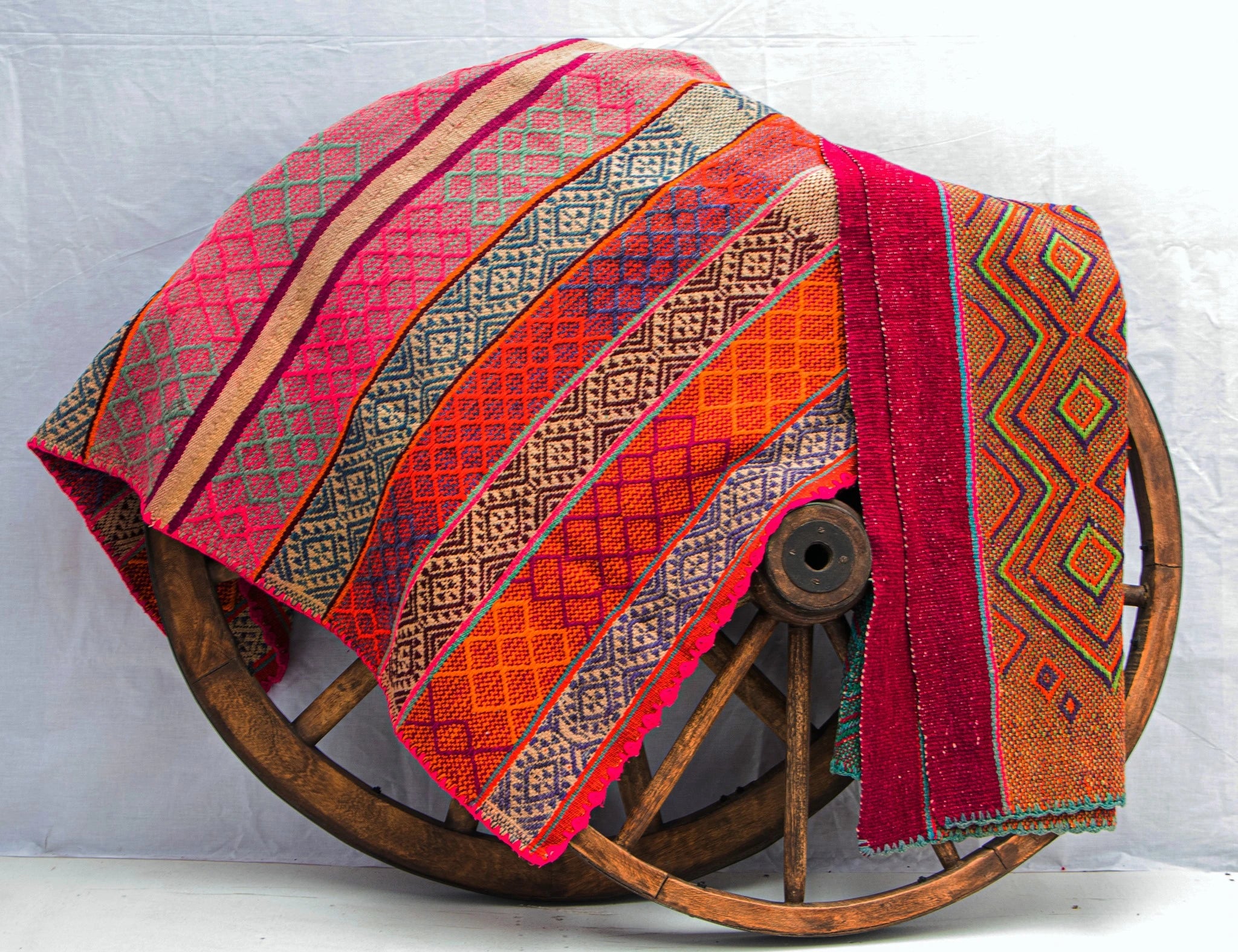 Peruvian vintage handwoven wool rugs with red and orange diamond patterns displayed on a wooden wheel