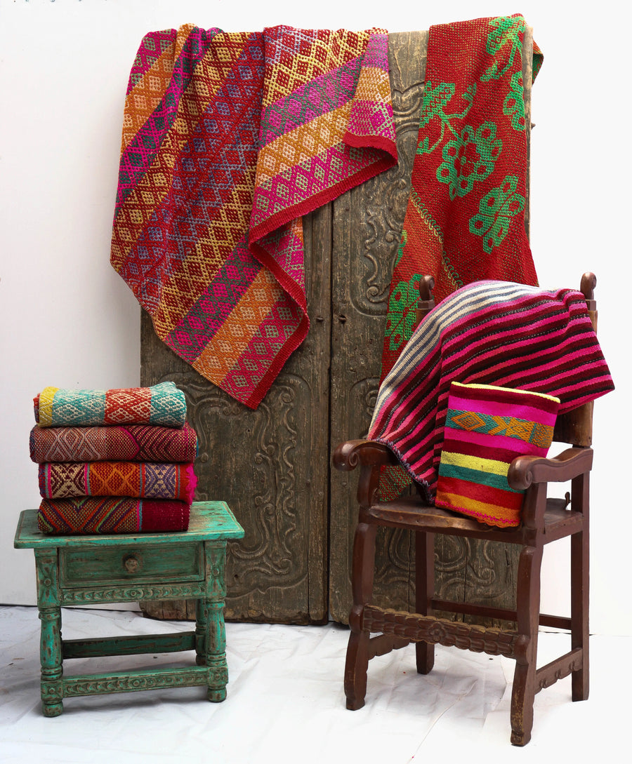 Colorful Peruvian handwoven vintage patterned wool frazadas and pillows stacked on rustic chair and stool